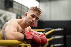 Athlete man boxer wearing boxing gloves resting on ropes in boxing ring at gym