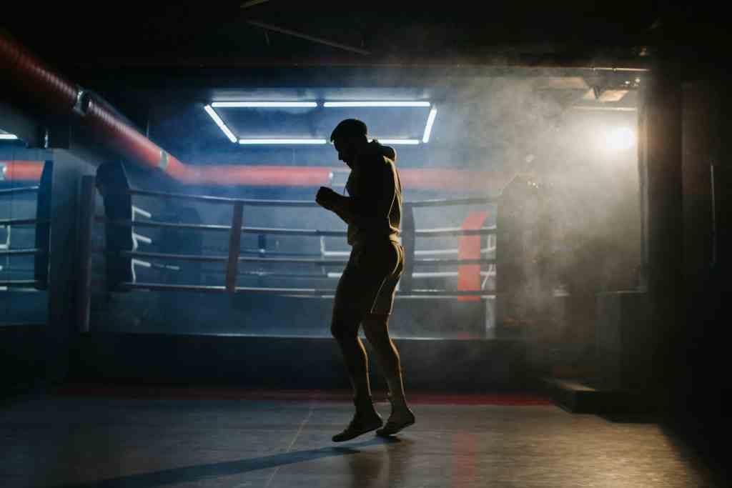 A male boxer is boxing with a shadow on the background of a boxing ring.