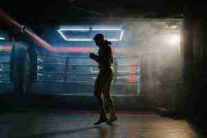 A male boxer is boxing with a shadow on the background of a boxing ring.