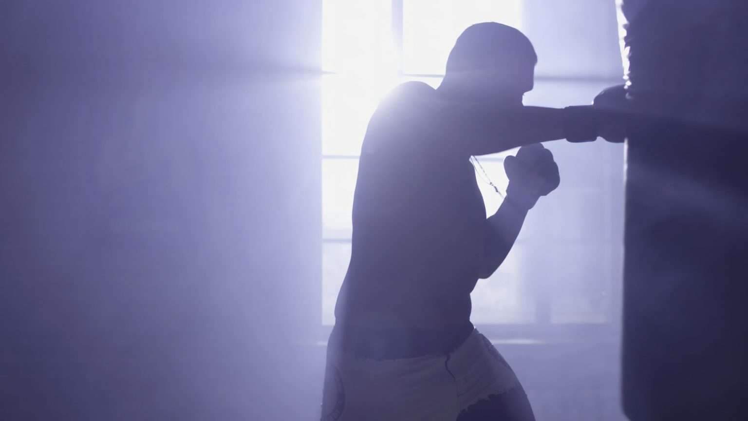 Muscular handsome fighter giving a forceful forward kick during a practise round with a boxing bag