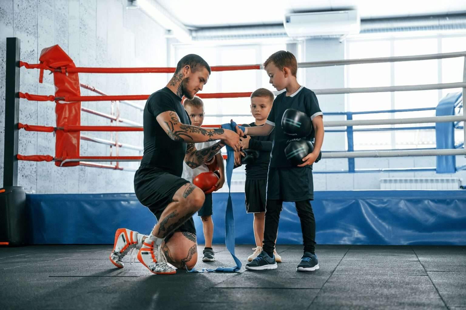 À quel âge commencer la boxe anglaise ? Wearing blue hand wraps. Young tattooed coach teaching the kids boxing techniques