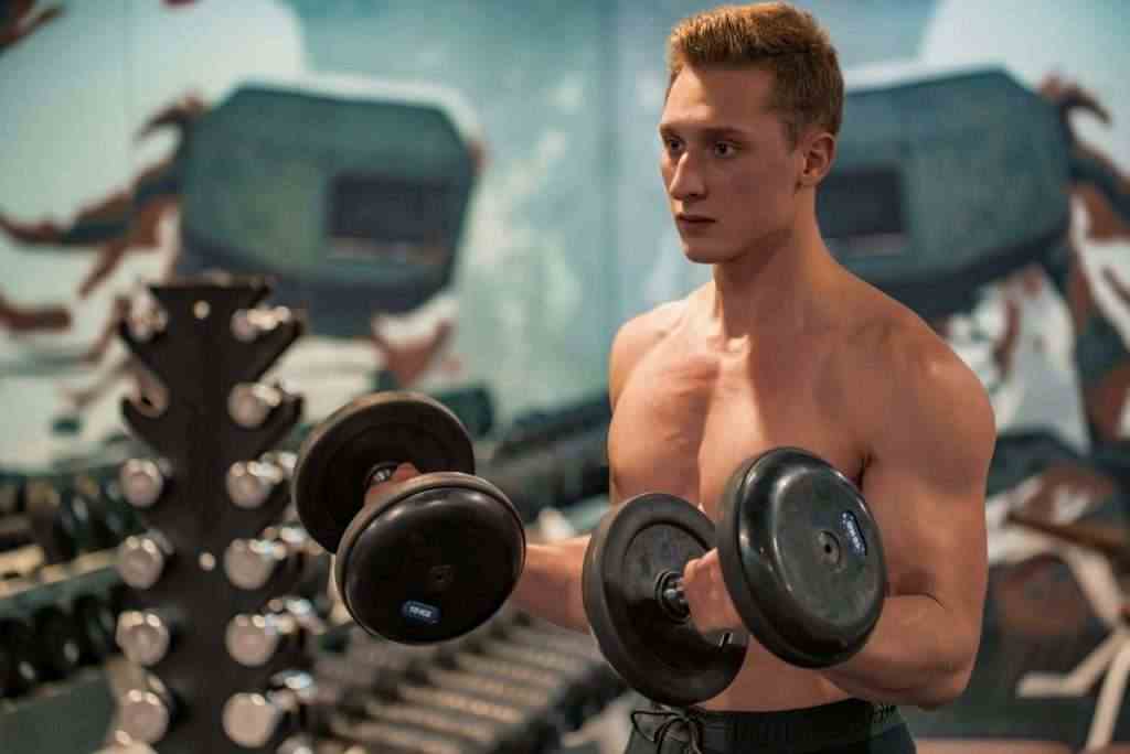 Attractive male athlete doing biceps exercise with dumbbells