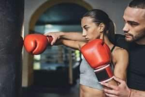 handsome young trainer training young female boxer with punching bag