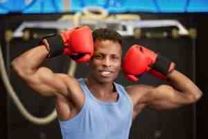 Muscular Black Boxer Showing Off Gloves in Gym
