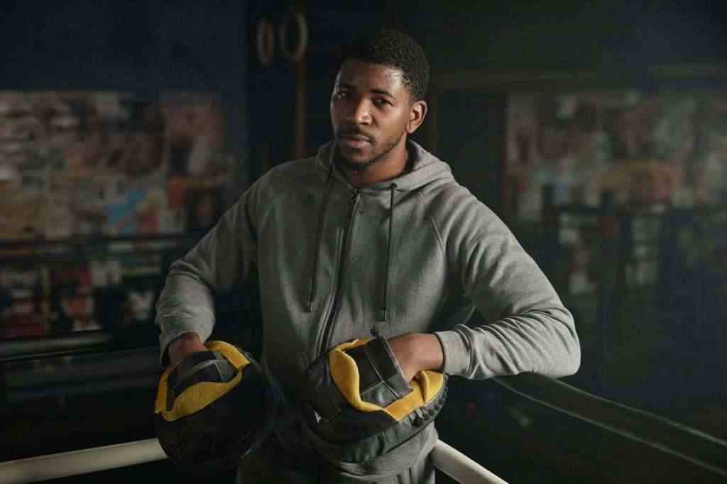 Young African American male boxing trainer in hoodie and pads