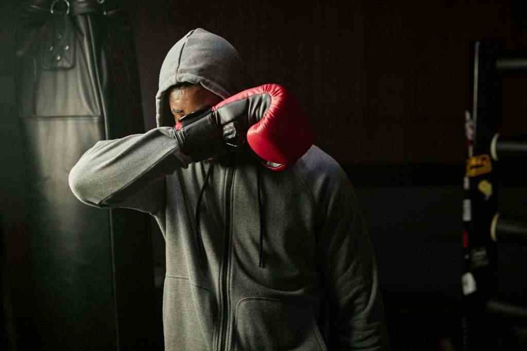 Young tired African American boxer in grey hoodie hiding his face