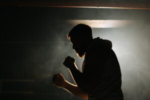 A male boxer is boxing with a shadow on the background of a boxing ring.