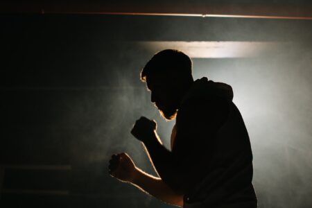 A male boxer is boxing with a shadow on the background of a boxing ring.