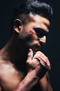 Injury, blood and man with a bandage from fighting or training for MMA or kickboxing in a dark stud