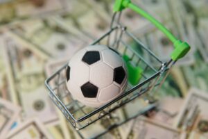 Soccer ball in shopping cart on usa dollar banknotes background. Football cup earnings.