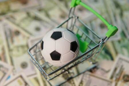 Soccer ball in shopping cart on usa dollar banknotes background. Football cup earnings.