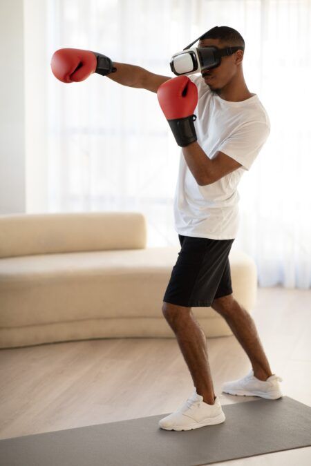 Young black sportsman in VR headset boxing at home