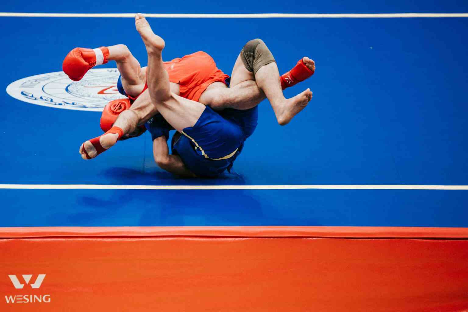 Two athletes engaged in an intense wrestling match on a blue mat.