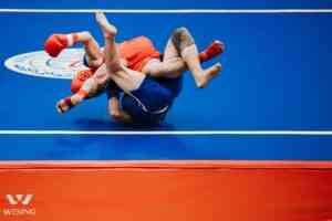 Two athletes engaged in an intense wrestling match on a blue mat.