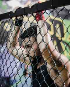 Focused athlete in sports gear holding a chain link fence at the gym, showcasing determination.