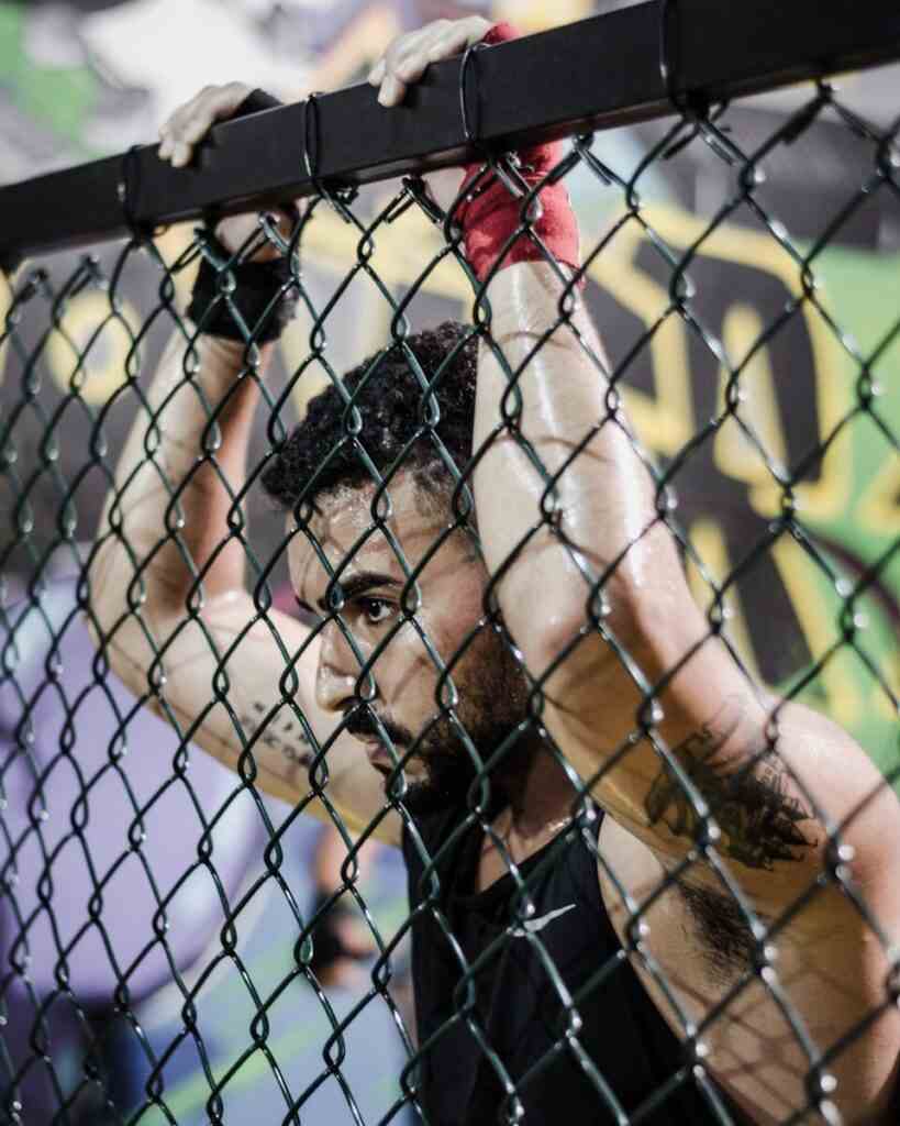 Strickland vs Hernandez : le combat qui va tout changer à l’UFC Focused athlete in sports gear holding a chain link fence at the gym, showcasing determination.